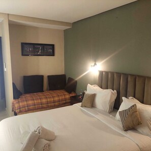 A hotel room with a large bed, a headboard with lights, a wall-mounted picture, and a nightstand with a bottle.