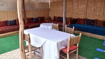 An outdoor seating area with a round table and chairs, surrounded by cushioned sofas and a decorative fence.