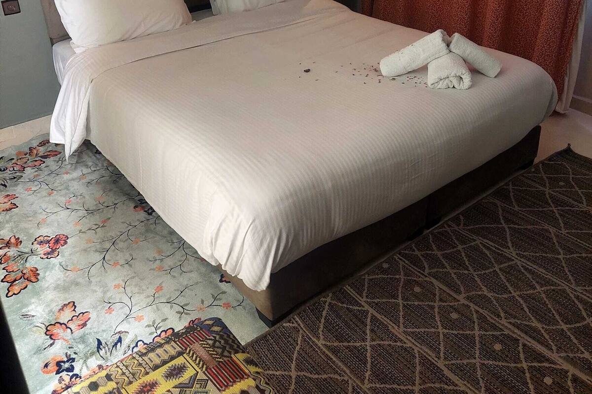 A hotel room with a large bed, a headboard, a wall-mounted light, and a patterned rug.