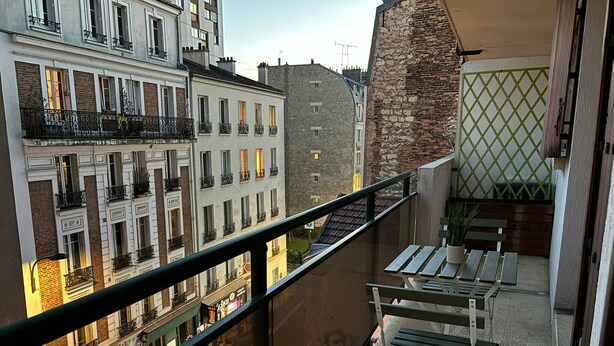 Ein Balkon mit Blick auf angrenzende Gebäude, eine kleine Sitzecke und eine grüne Rankgitterwand.