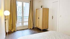 Ein Schlafzimmer mit einem Bett, einem Kleiderschrank, einem Fenster mit Vorhängen und einer Lampe.