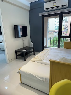 A modern hotel room with a bed, a TV, a small table, and an air conditioning unit. - 1BR End Unit with 1.5 Bath, Private Balcony, Pool Access,Designated Free Parking (Metro Manila)