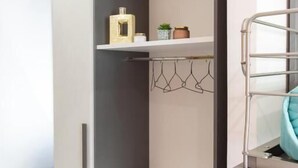 Ein kleiner Raum mit integriertem Kleiderschrank, einer kleinen Ablagefläche mit Dekoration und einem Metallgestell mit einem Handtuch.