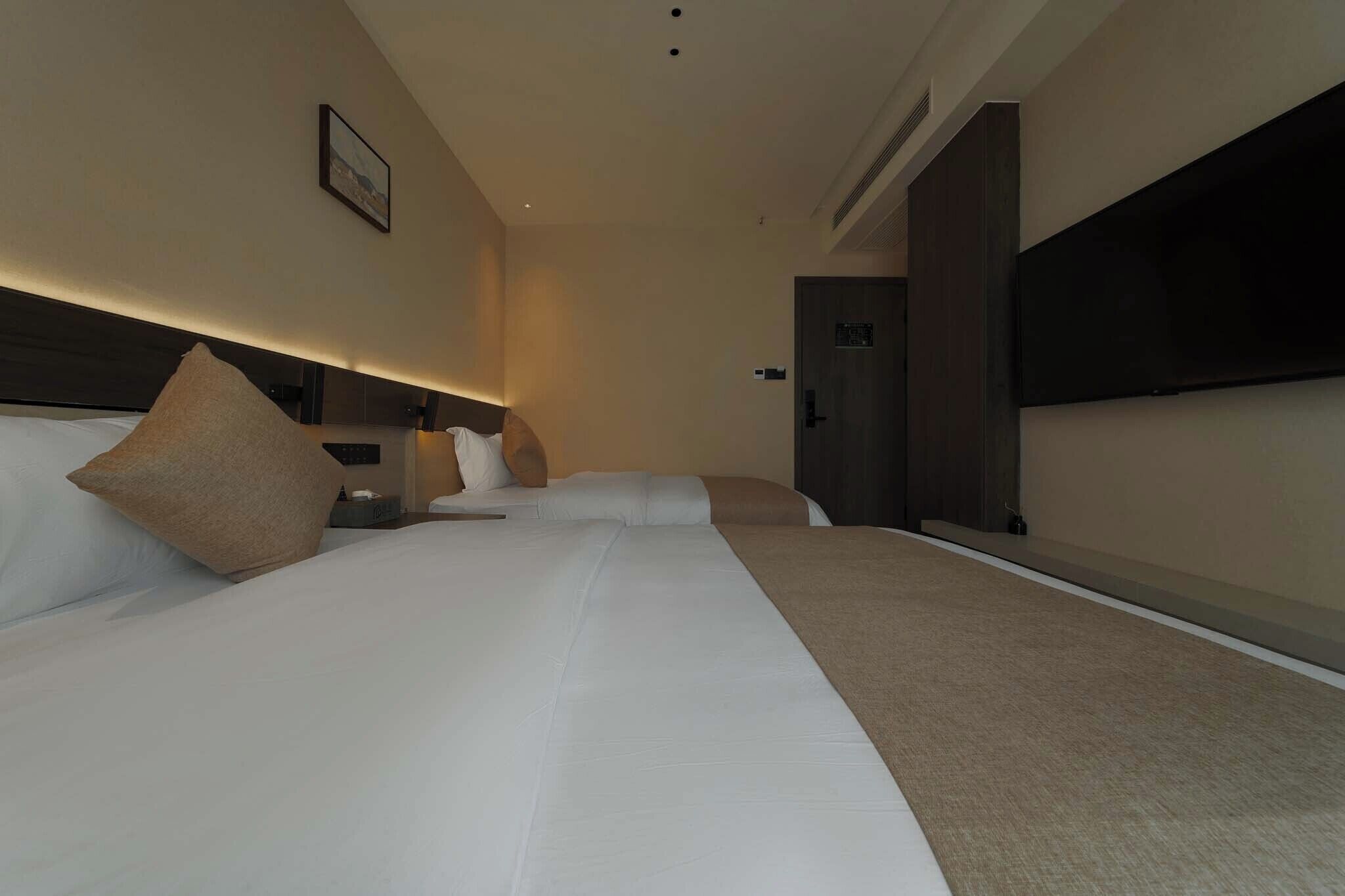 Une chambre d’hôtel avec un grand lit, un téléviseur à écran plat, une table de chevet et une porte donnant sur un couloir.