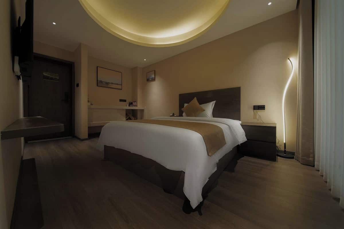 Een moderne hotelkamer met een groot bed, nachtkastjes, een bureau en een plafondlamp.