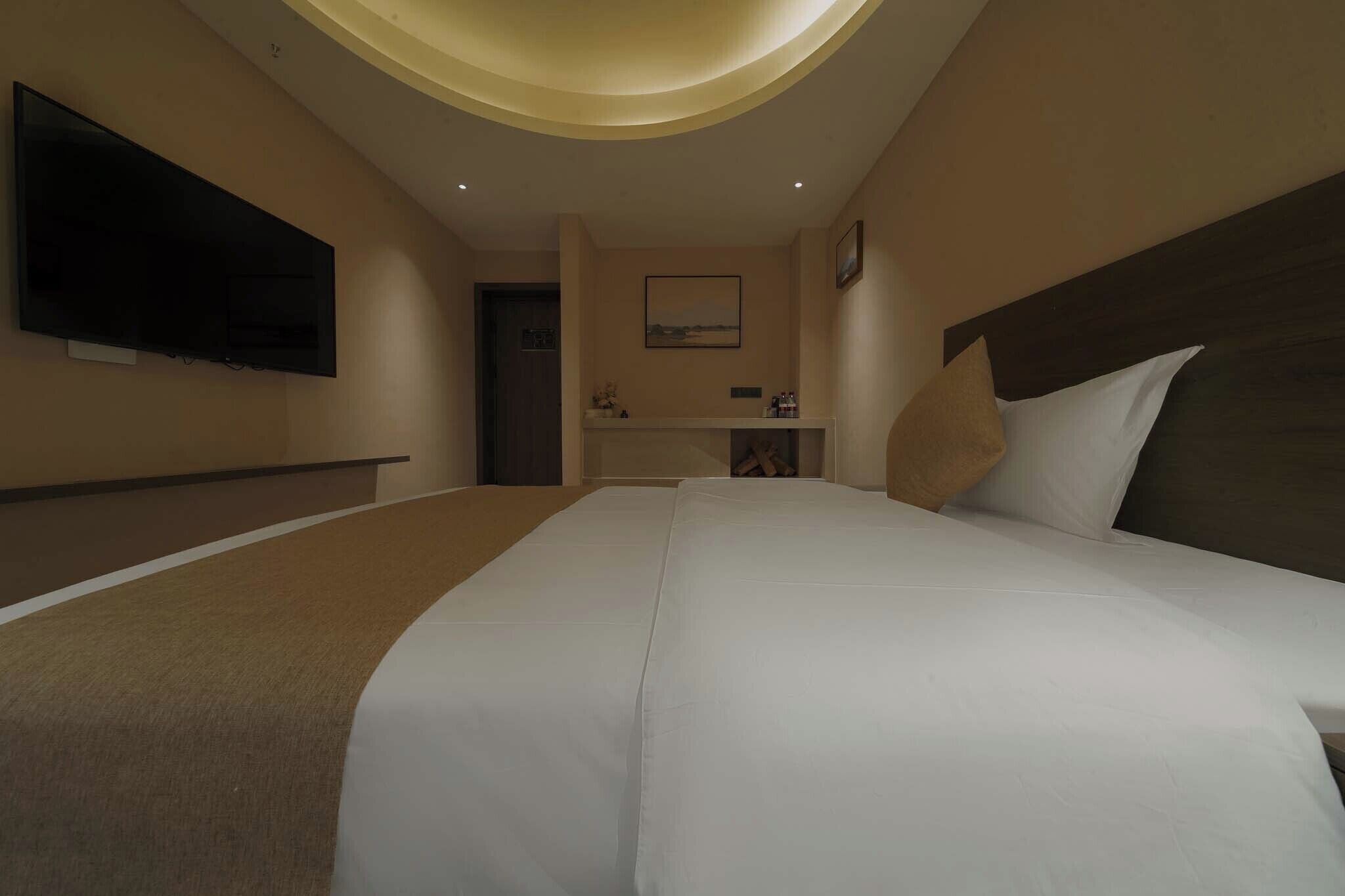 Habitación de hotel con una cama grande, un televisor de pantalla plana montado en la pared, una mesita de noche pequeña y un cuadro enmarcado.