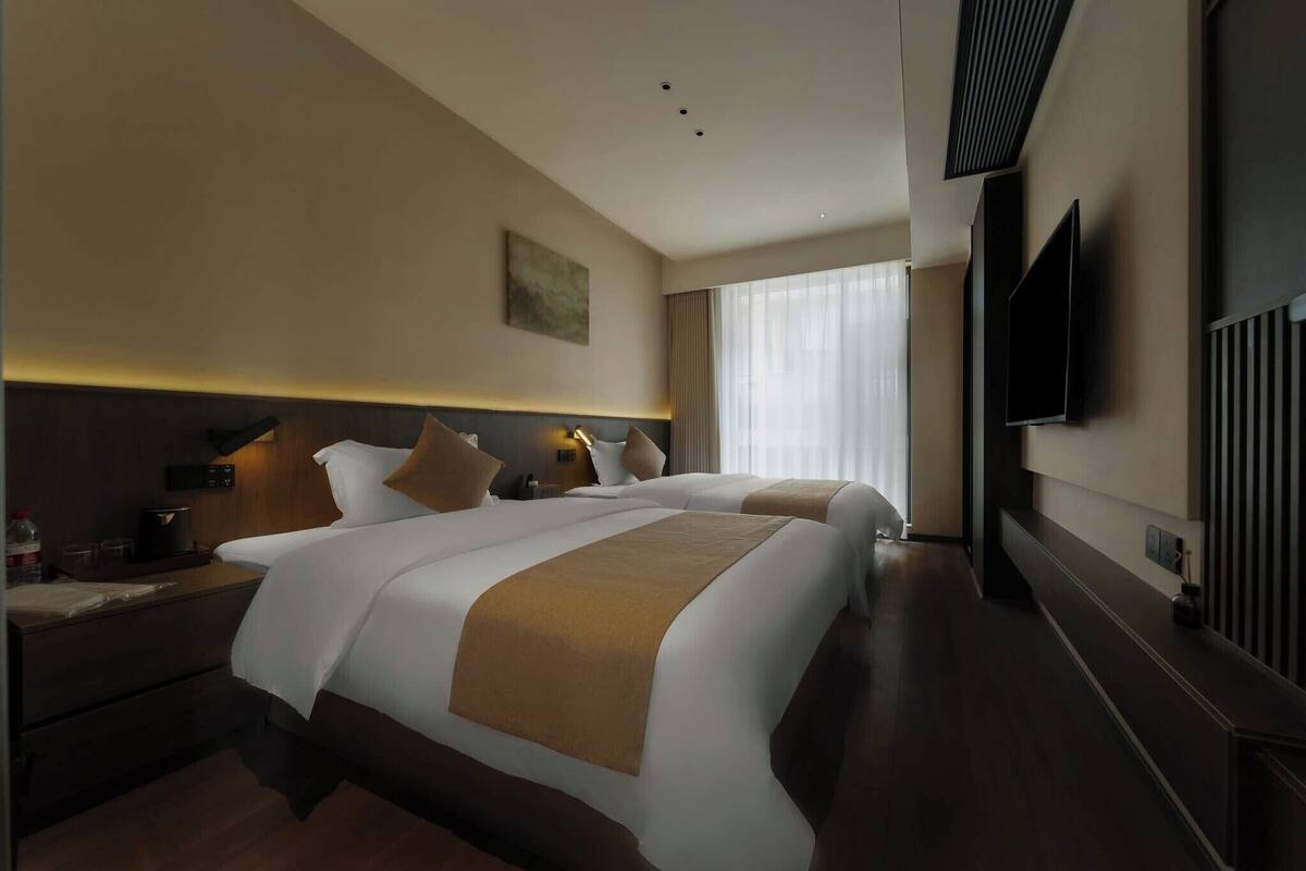 Hotelkamer met twee bedden, een wandtelevisie en een groot raam met gordijnen.