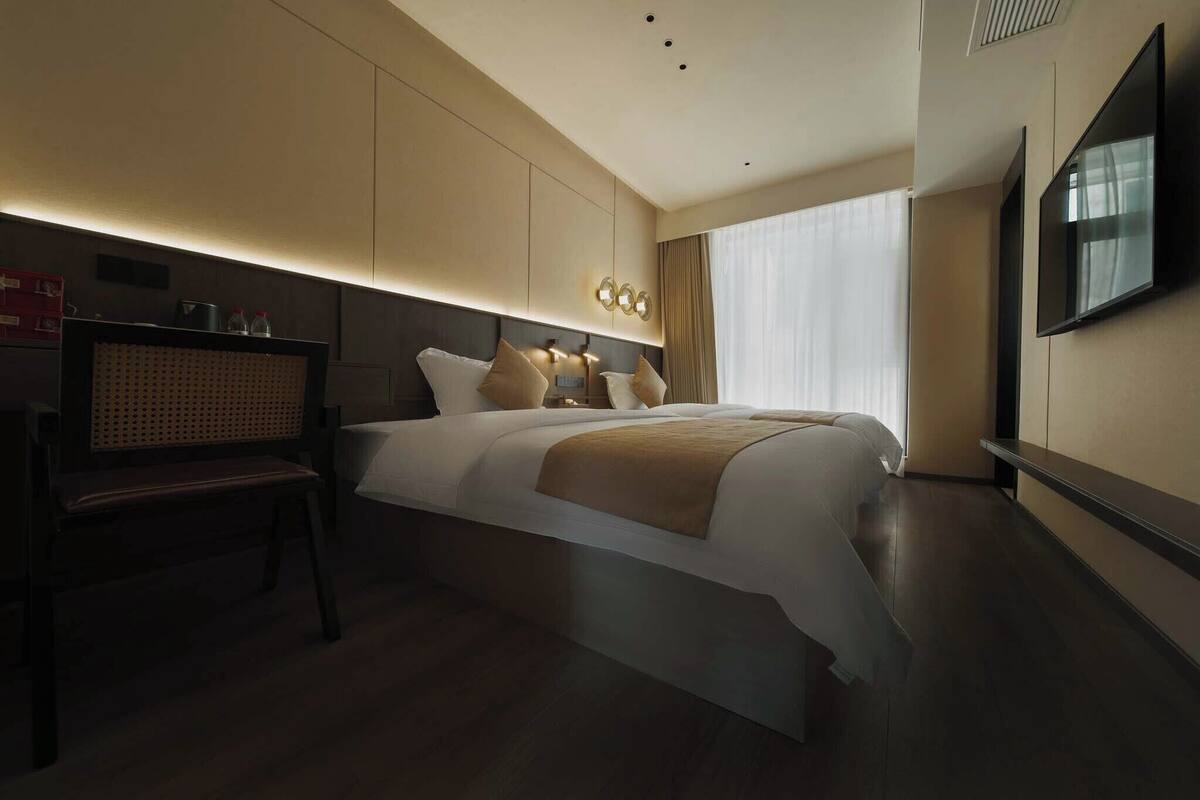 Een moderne hotelkamer met een groot bed, bedlampen, een flatscreen televisie en een zithoek met een houten bank.