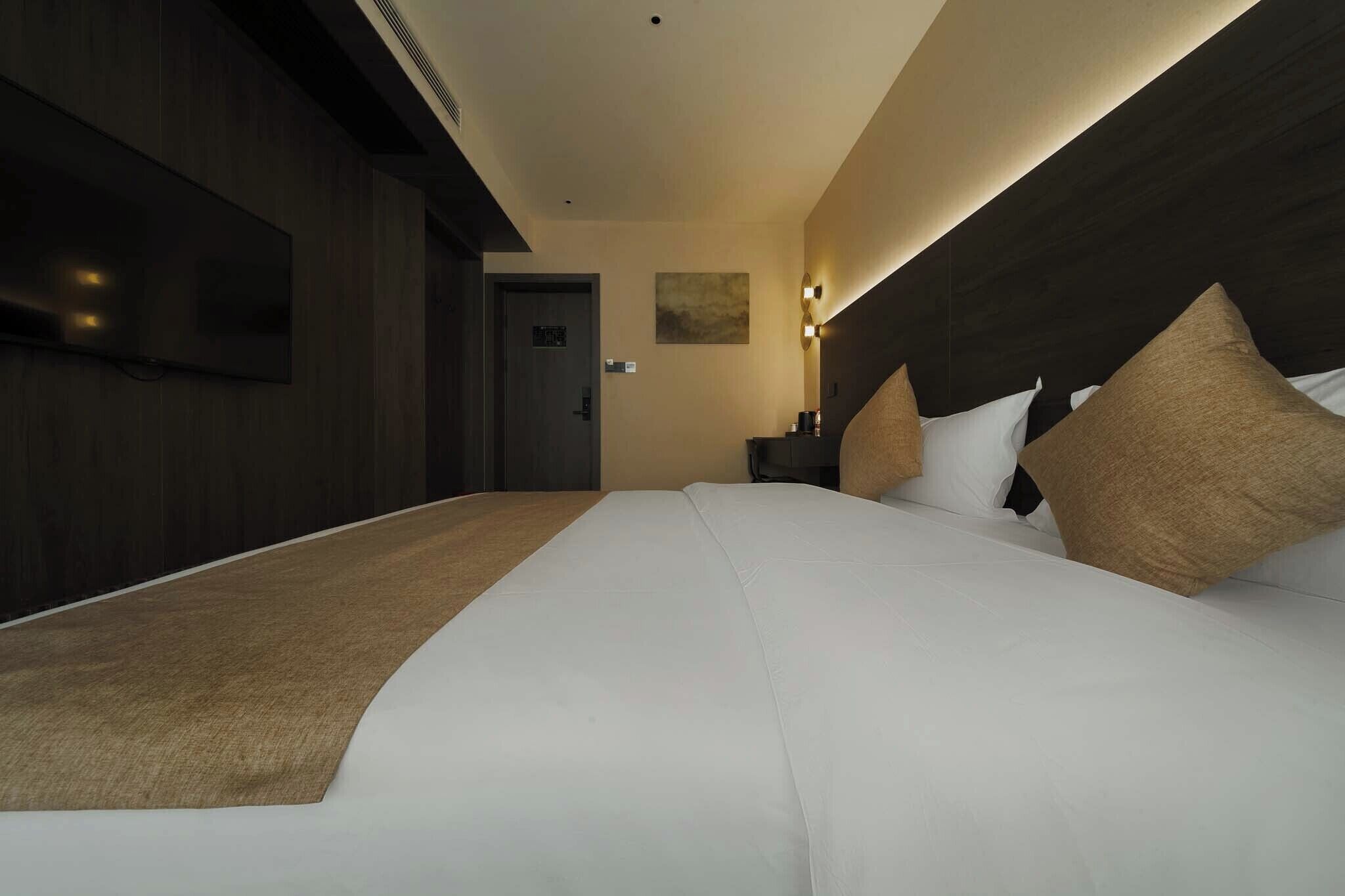 Una habitación de hotel moderna con una cama grande, un televisor de pantalla plana en la pared y una mesita de noche con lámpara.