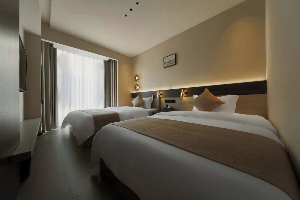 Een hotelkamer met twee bedden, een televisie, een bureau en een groot raam met gordijnen.