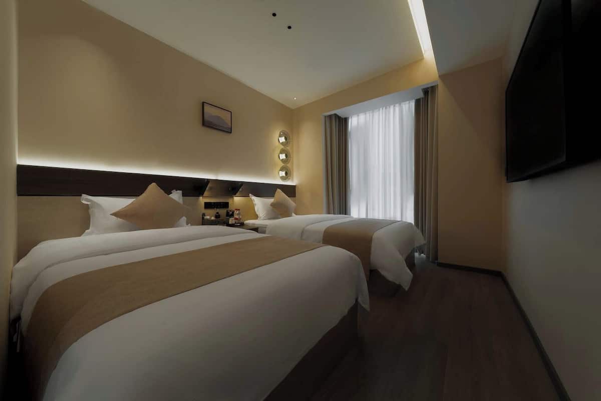 Een hotelkamer met twee bedden, een flatscreen televisie aan de wand en een groot raam met gordijnen.