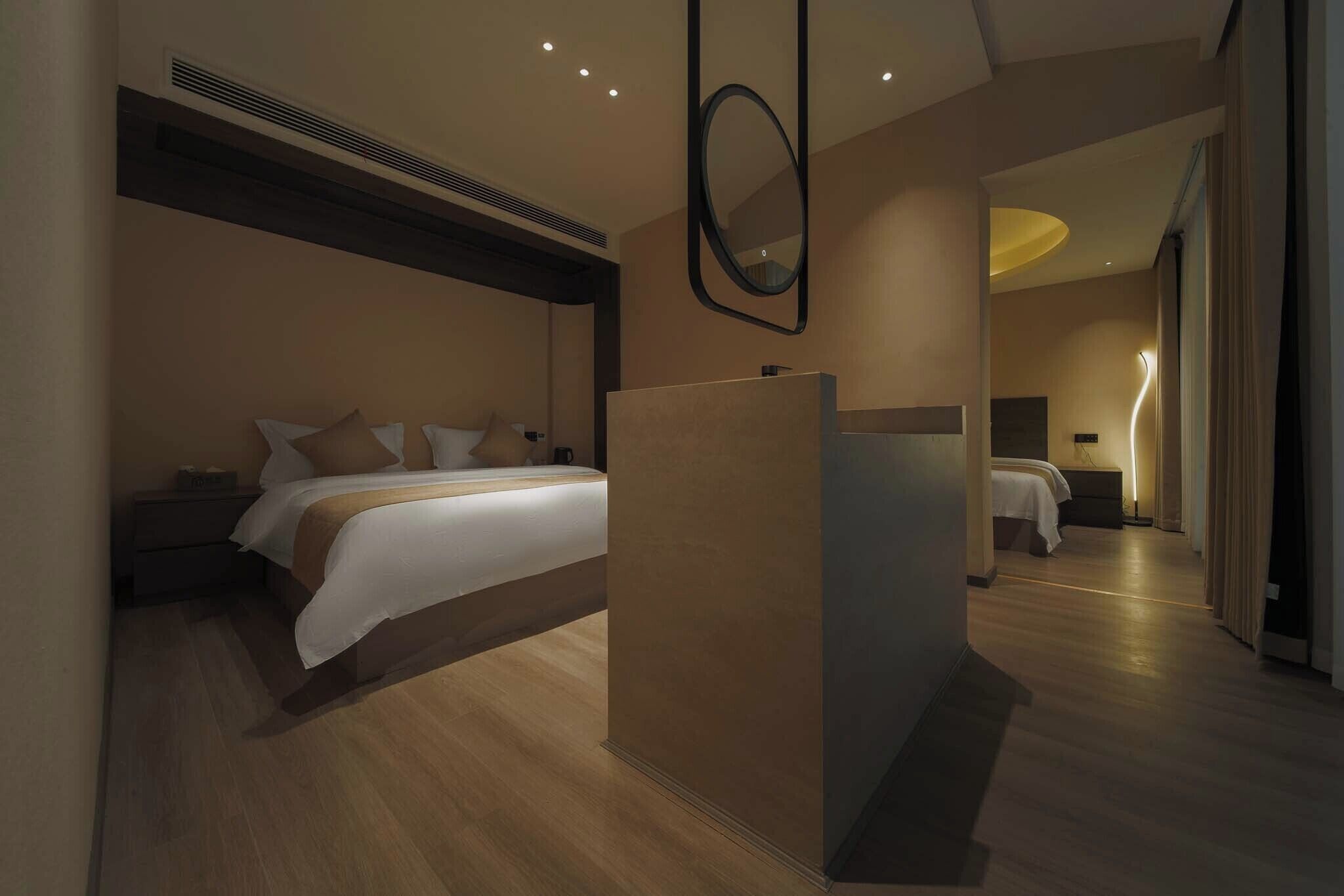A modern hotel room with a large bed, a bedside table, a mirror, and a separate sleeping area.