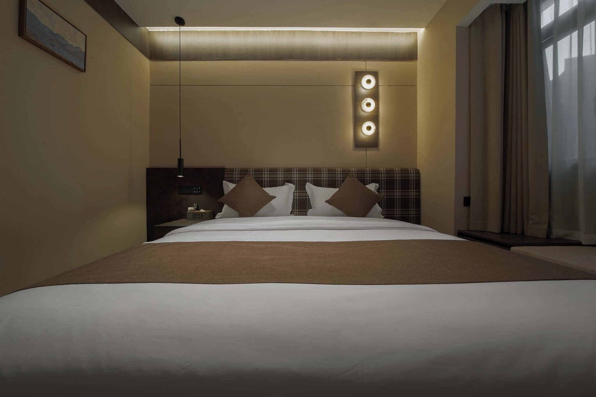 A hotel room with a large bed, a headboard with built-in lighting, a bedside table, and a window with curtains.
