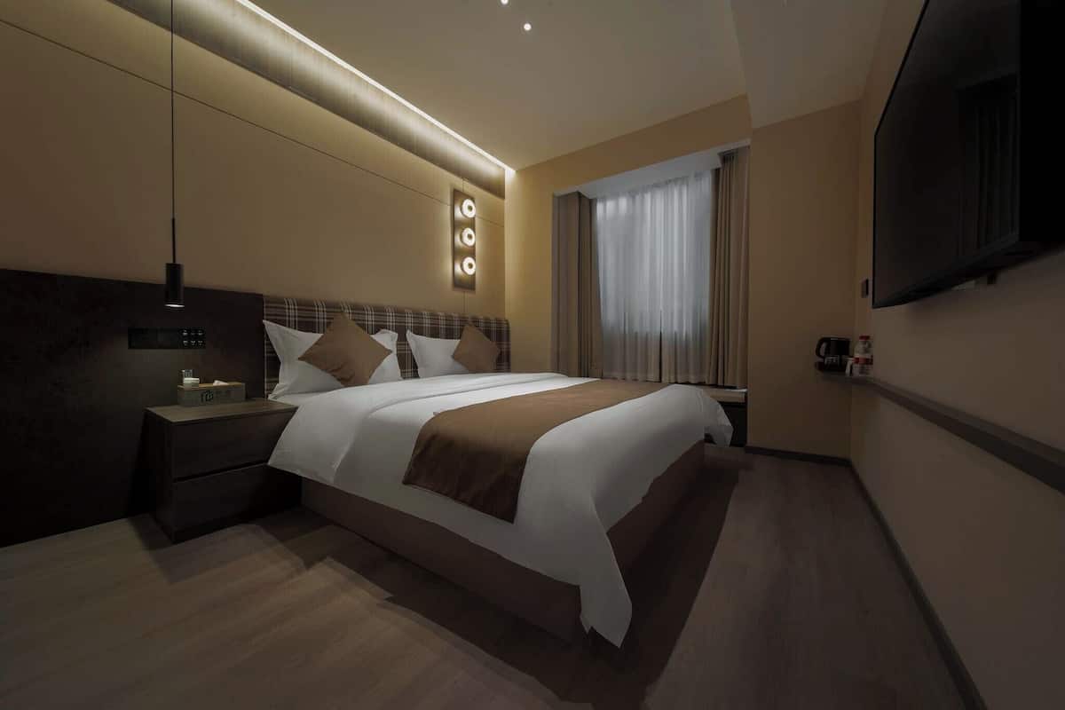 Een moderne hotelkamer met een groot bed, nachtkastjes, een flatscreen televisie en een raam met gordijnen.