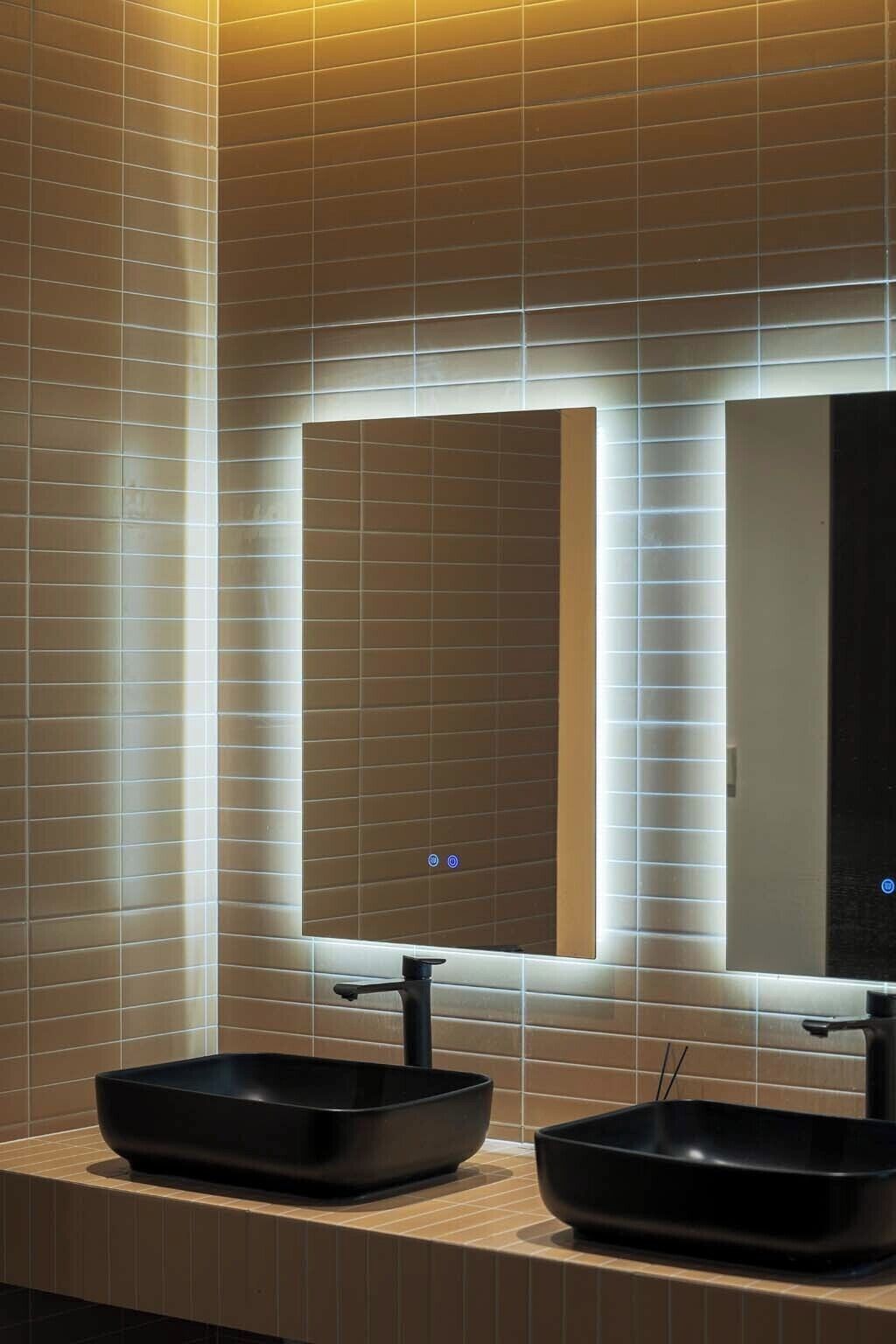 Un baño con dos lavamanos negros y un espejo con bordes iluminados.