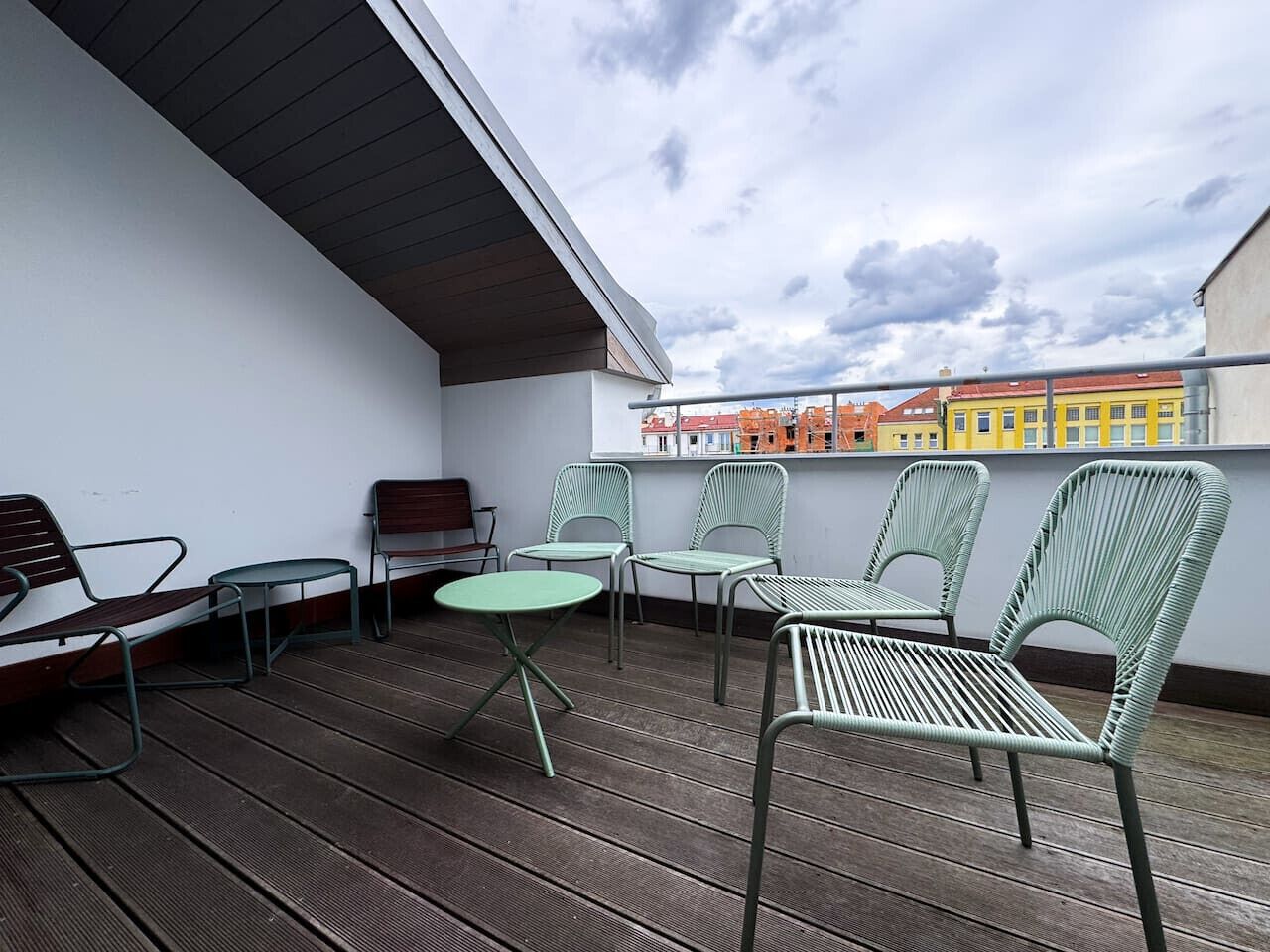 Una terrazza sul tetto con sedie in metallo e un tavolino, con vista su un paesaggio urbano pieno di edifici colorati.