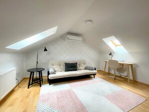 Ein Loft-Zimmer mit einer Couch, einem kleinen Tisch, einem Schreibtisch und einem Dachfenster.