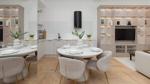 Eine moderne Küche mit weißen Schränken, einem runden Esstisch gedeckt mit Tellern und Gläsern sowie einem in die Wand eingelassenen Fernseher über der Arbeitsfläche.