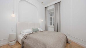 Ein schlicht eingerichtetes Schlafzimmer mit einem großen Bett, einem Nachttisch und einem Fenster mit Vorhängen.