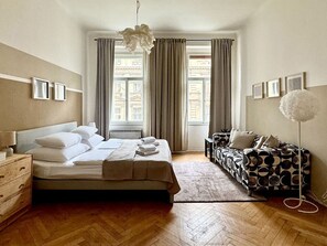 Un dormitorio con cama, sofá, lámpara de pie y ventana con cortinas.