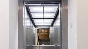 An elevator with a metallic interior, a glass door, and a tiled floor. - 3 bedroom apartment in Vinohrady (Prague 2)