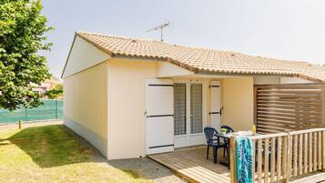 Un petit bâtiment d’un seul étage, doté d’un toit en tuiles, d’une terrasse en bois et d’un espace extérieur abrité avec une table et des chaises.