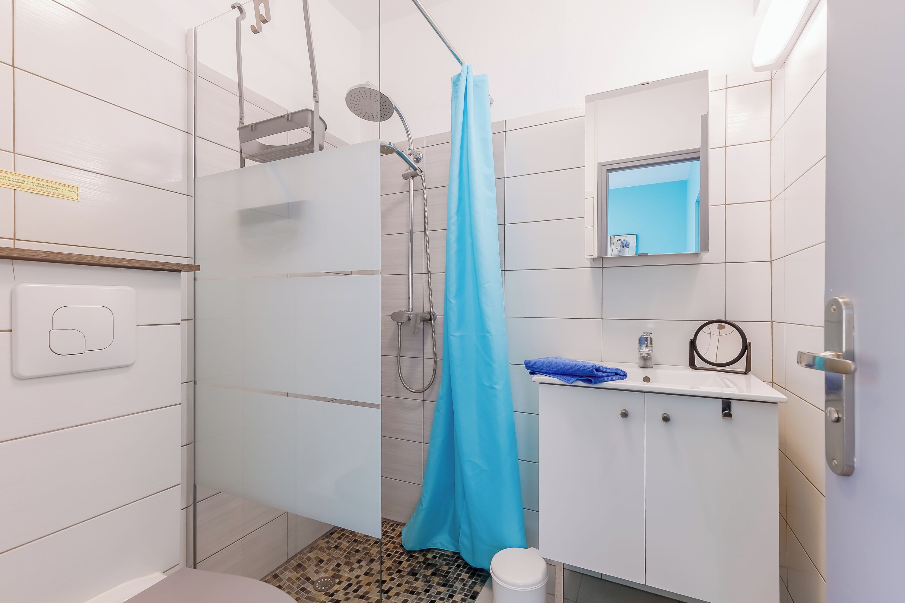 Ein modernes Badezimmer mit einer Duschkabine aus Glas, einem weißen Waschbecken mit Spiegel und einem blauen Handtuch auf der Ablagefläche.