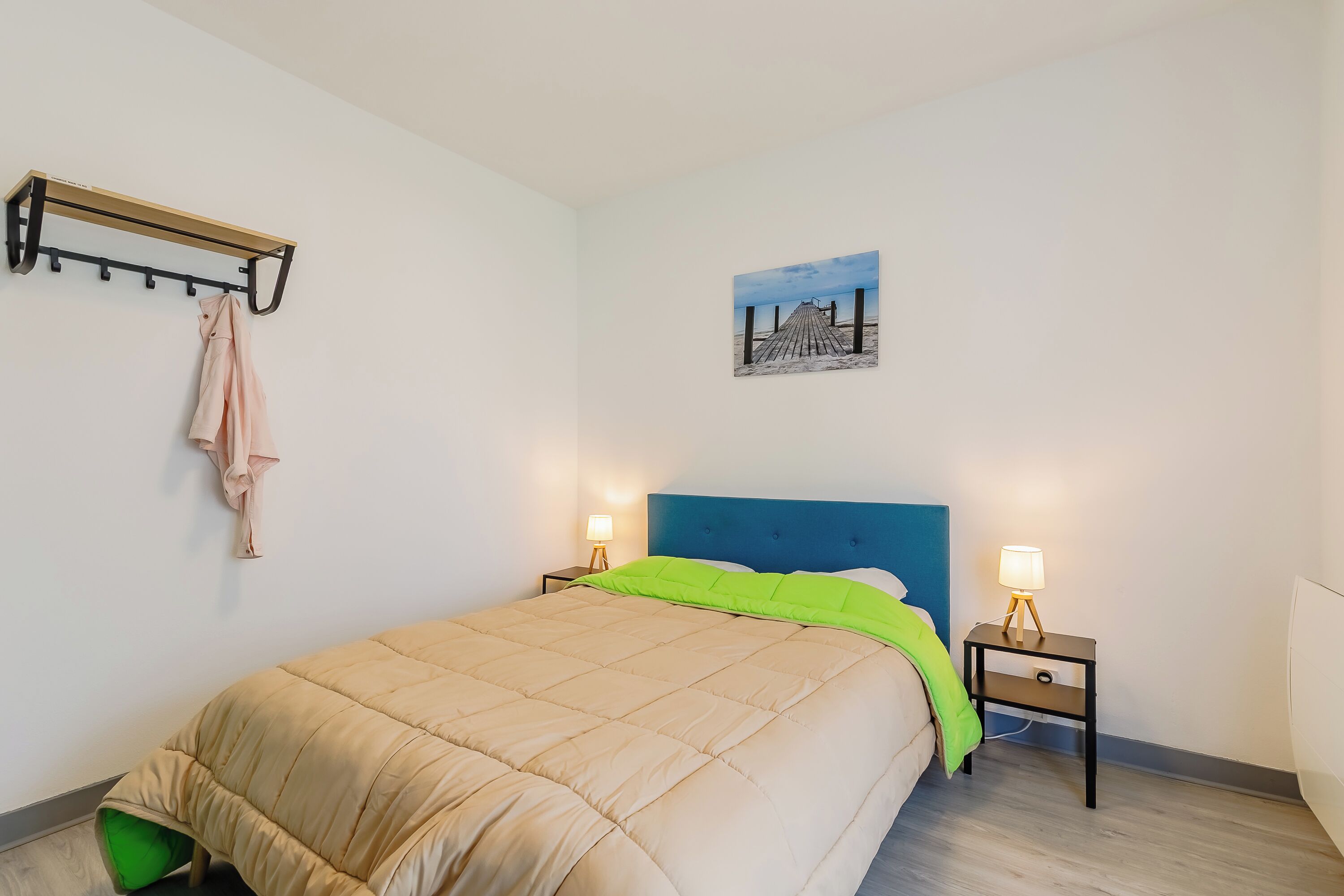 A bedroom with a bed, a headboard, a nightstand, a lamp, a coat rack, and a painting on the wall.