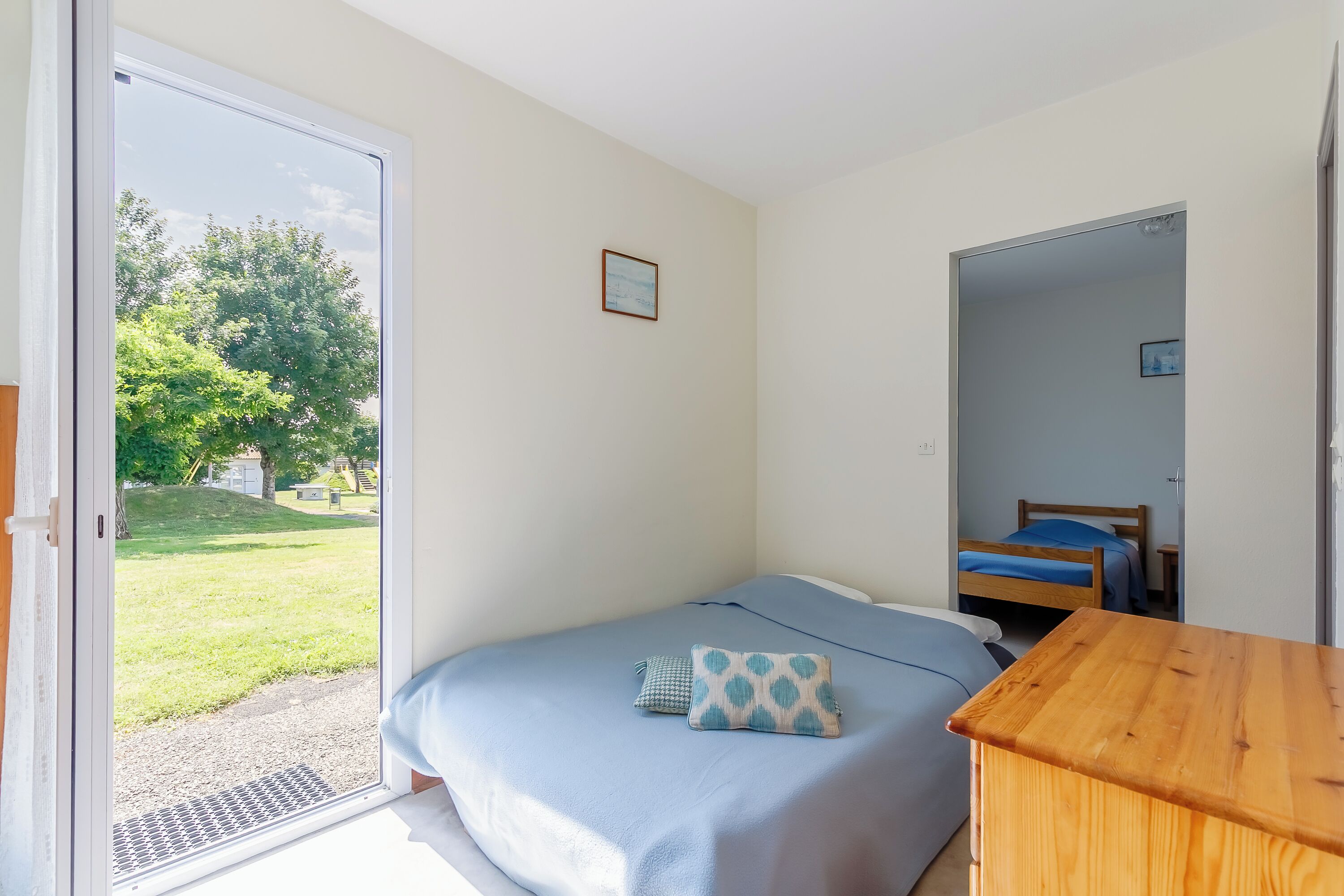 Een slaapkamer met een bed, een houten nachtkastje en uitzicht op een grasveld door een schuifdeur.