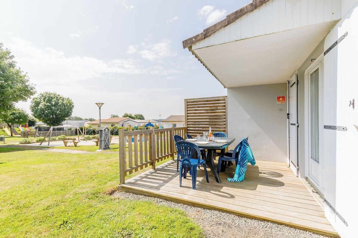 A covered outdoor patio with a table and chairs, a wooden deck, and a view of the surrounding area.