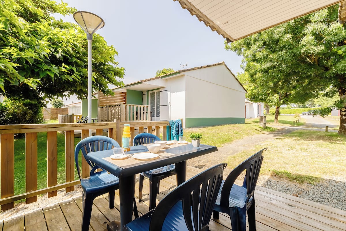 A wooden deck with a table and chairs, a lamp, and a small house in the background.