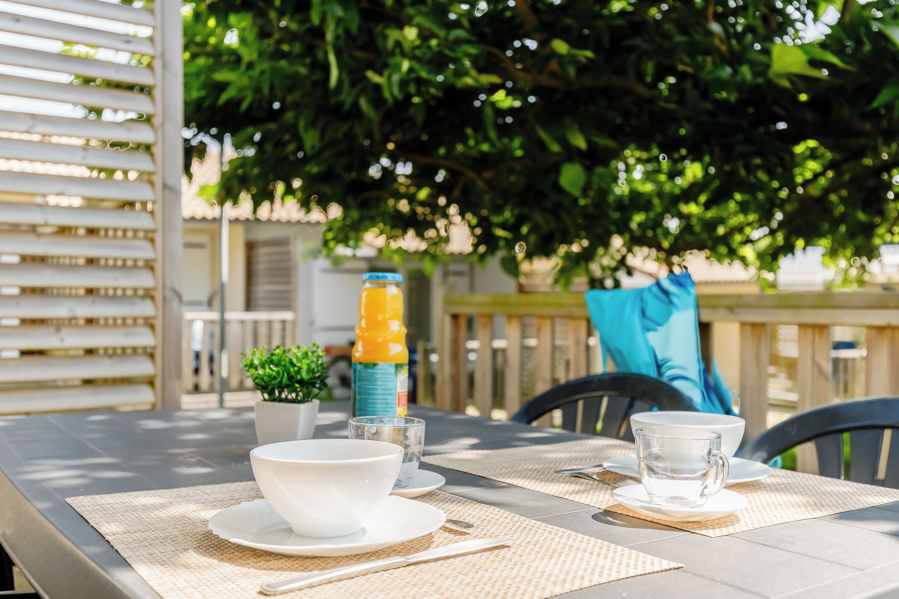 An outdoor dining table with a white bowl, a glass, and a bottle of juice.