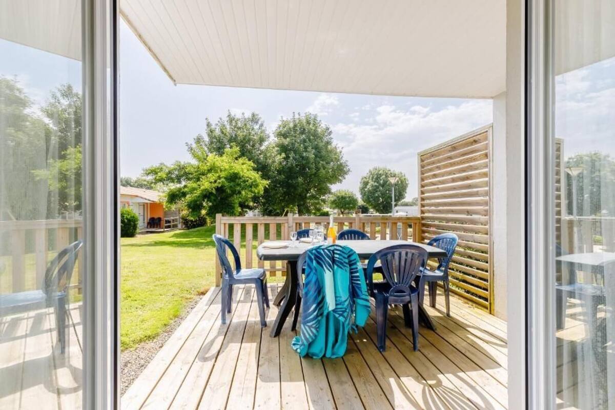A patio with a table and chairs, a wooden deck, and a view of a backyard with trees and a fence.