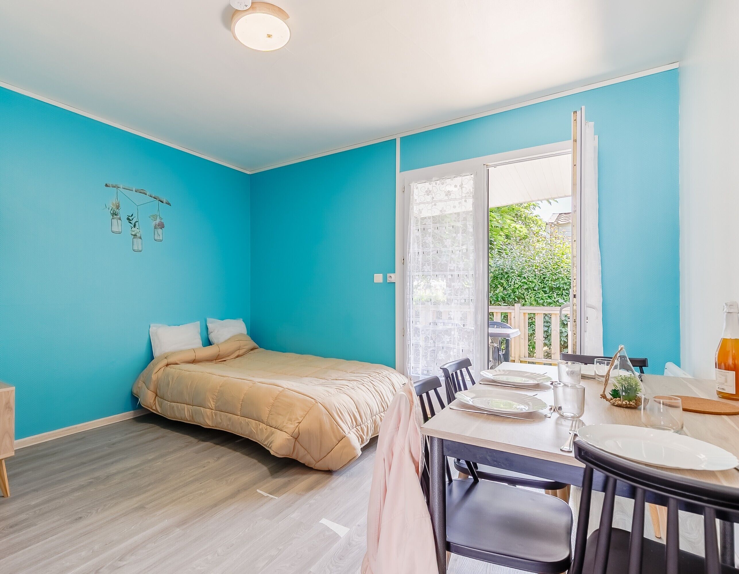 Una habitación con cama, una mesa de comedor con sillas y vistas a un balcón con vegetación.