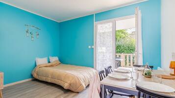 Una habitación con cama, una mesa de comedor con sillas y vistas a un balcón con vegetación.