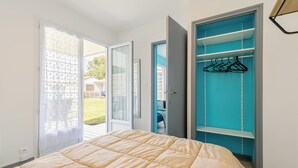 A bedroom with a bed, a sliding glass door leading to a balcony, and a blue closet with hanging space. - Village Vacances Gîtes Les Rivières (Maché)