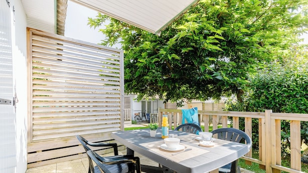 An outdoor patio with a table set for dining, surrounded by chairs, and a wooden fence. - Village Vacances Gîtes Les Rivières (Maché)