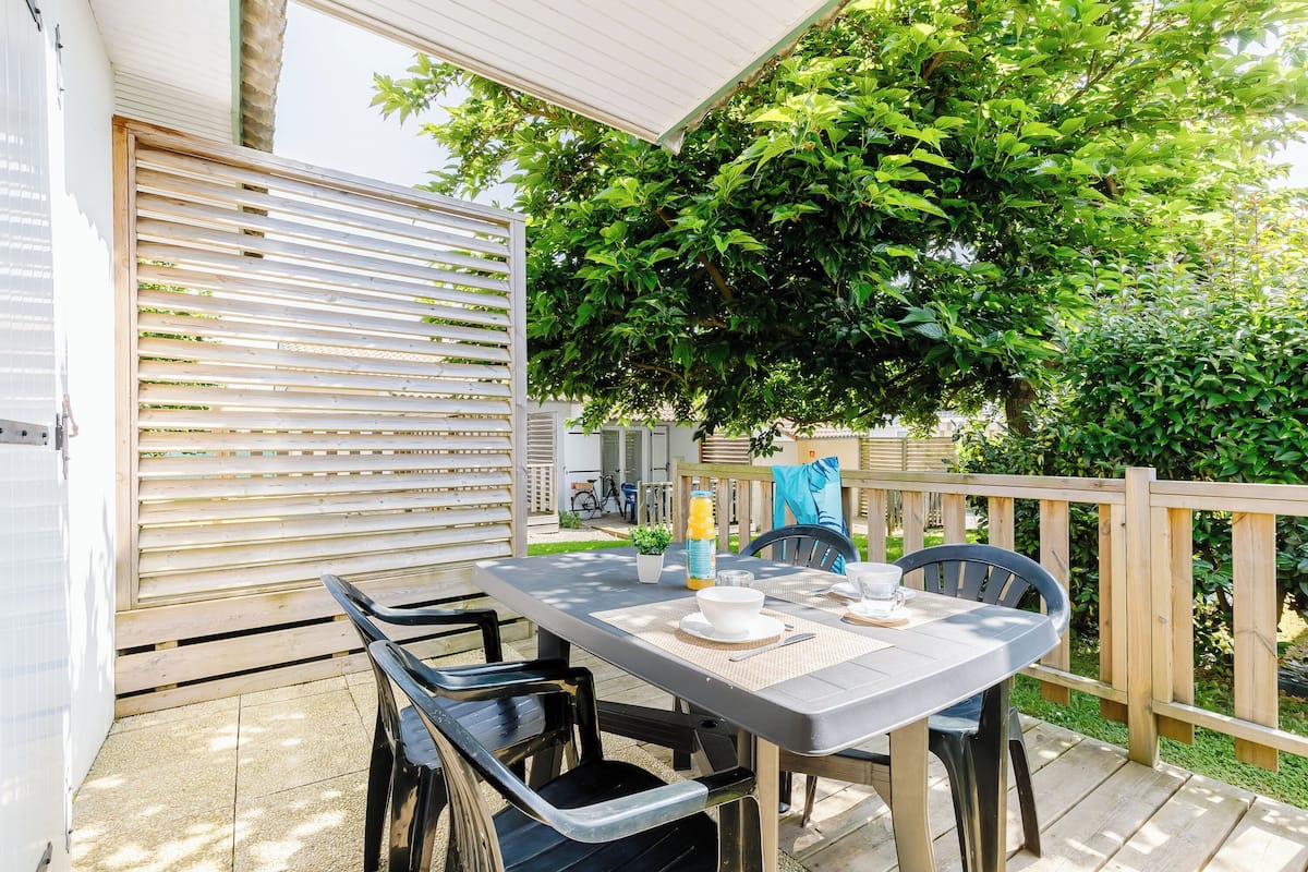 An outdoor patio with a table set for dining, surrounded by chairs, and a wooden fence.