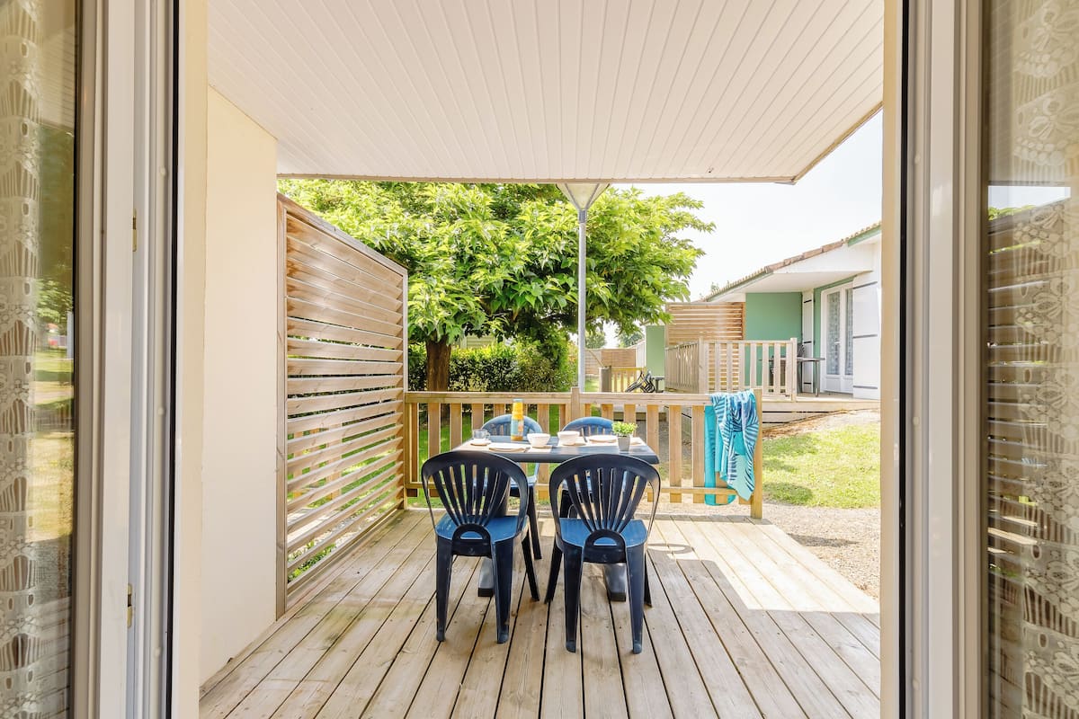 A covered patio with a table and chairs, a wooden fence, and a view of a house in the background.
