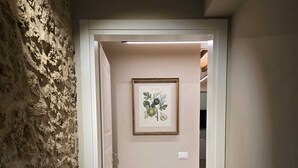 Un couloir avec un mur à texture, une illustration botanique encadrée et une porte donnant sur une autre pièce.