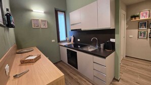 Une cuisine de taille réduite avec un plan de travail noir, des placards blancs et une table à manger en bois.