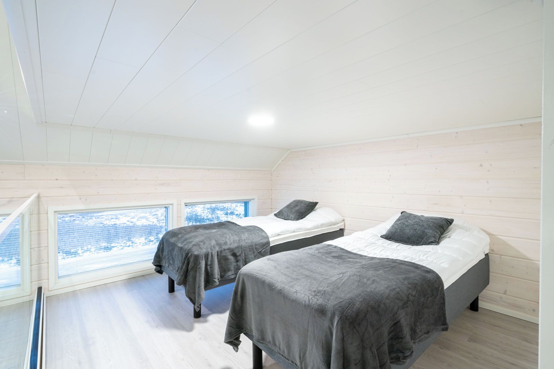 A bedroom with two beds, wooden walls, and large windows.