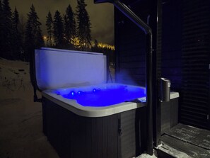 Una vasca idromassaggio con luce blu, circondata da neve e alberi.