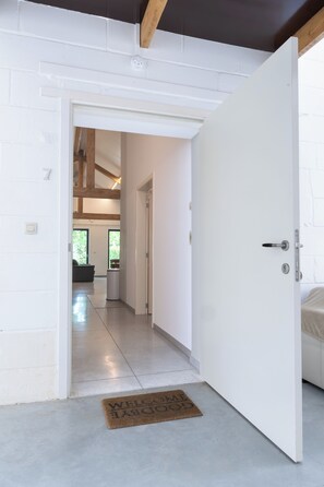 A hallway leading to a room with a white door, a doormat, and a visible window. - Landlord  (Holsbeek)