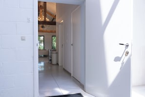 A hallway with a white door, a light switch, and a trash bin. - Landlord (Holsbeek)