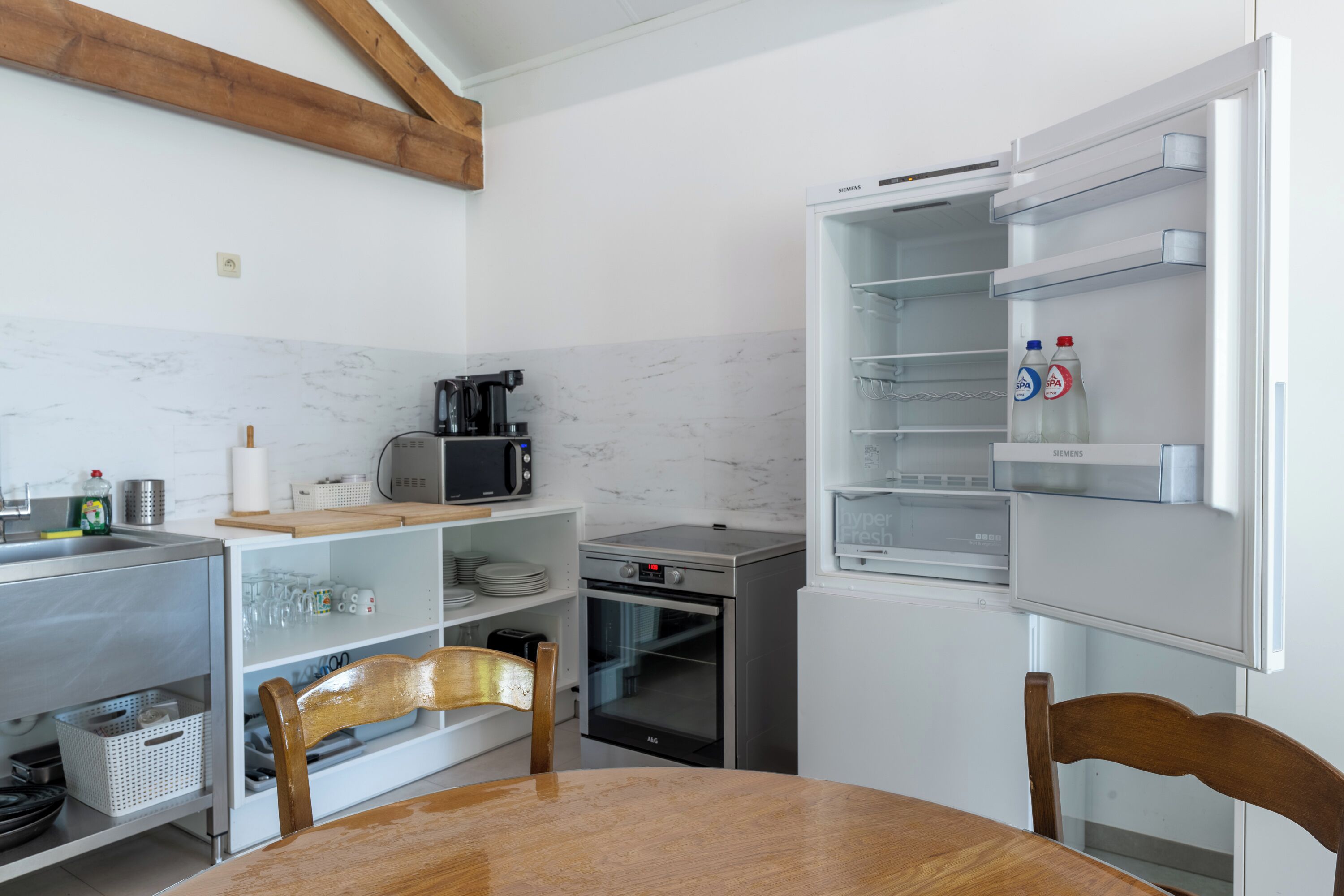 A compact kitchen with a refrigerator, microwave, toaster, and a wooden dining table.