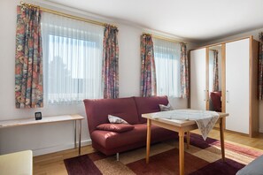 A room with a sofa, a small table, a mirror, and a window with curtains. - Room with Shared Garden and Wi-Fi (Kressbronn am Bodensee)