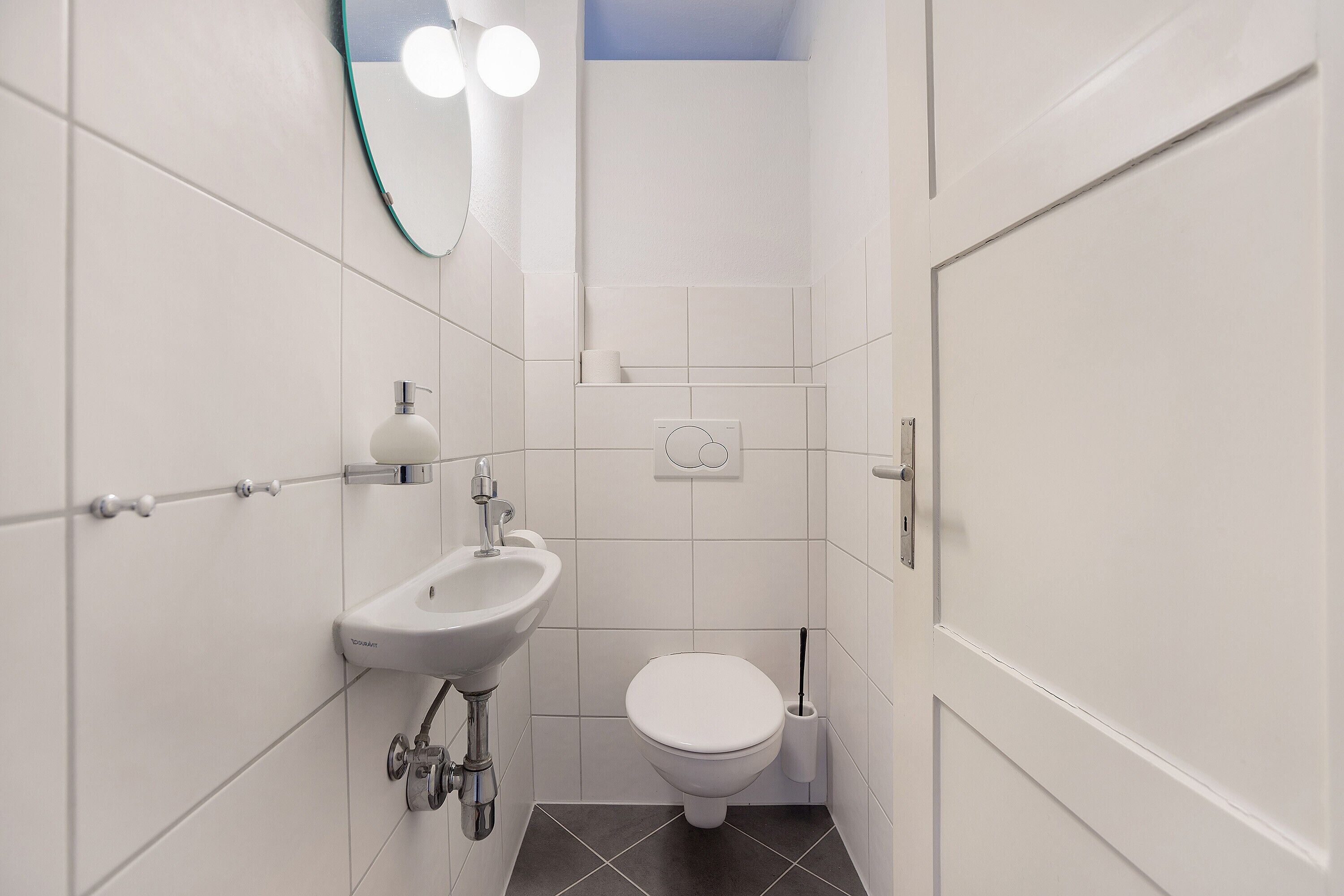 Une salle de bain avec un lavabo, des toilettes et un miroir, le tout de couleur blanche.