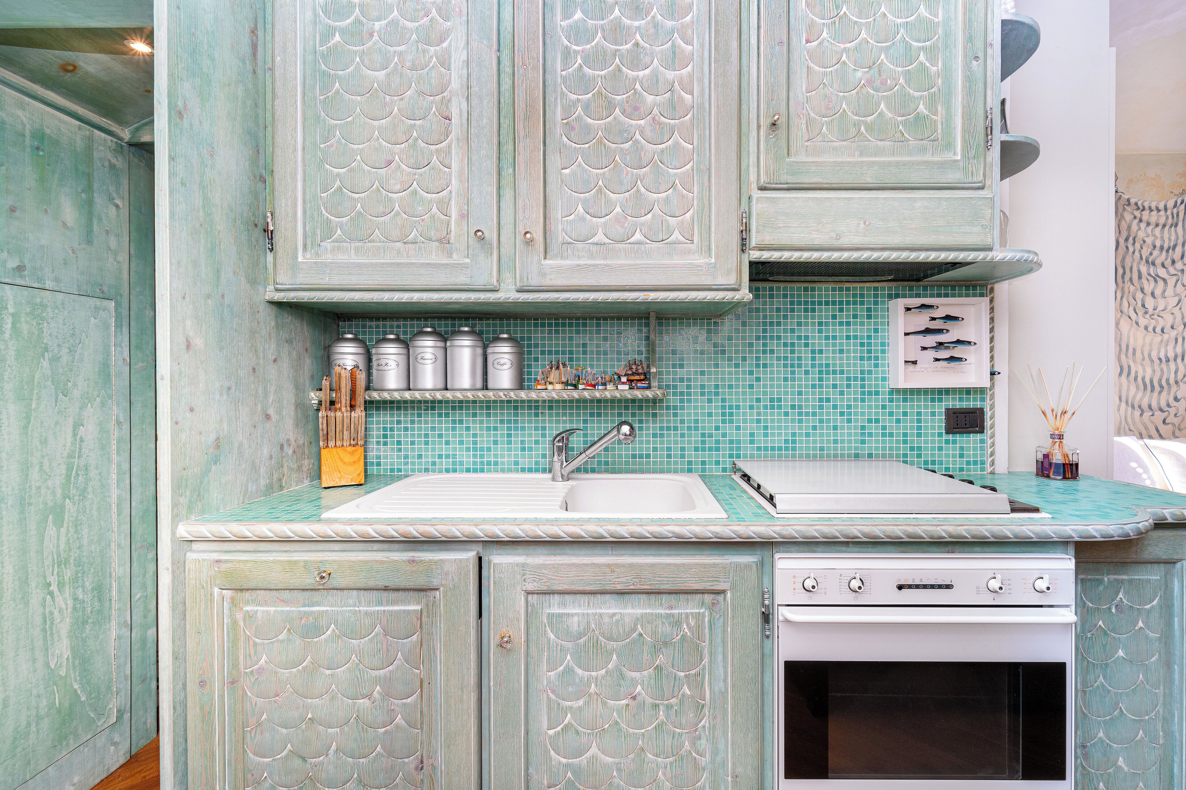 A kitchen with teal cabinetry, a white sink, and a built-in oven.