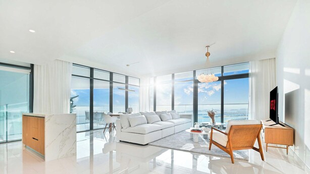 A modern living room with a white sofa, a coffee table, and a TV. There is a large window offering a view of the sky and clouds. - LUX ULTRA Luxury Palm Dubai Eye Suite (Dubai)